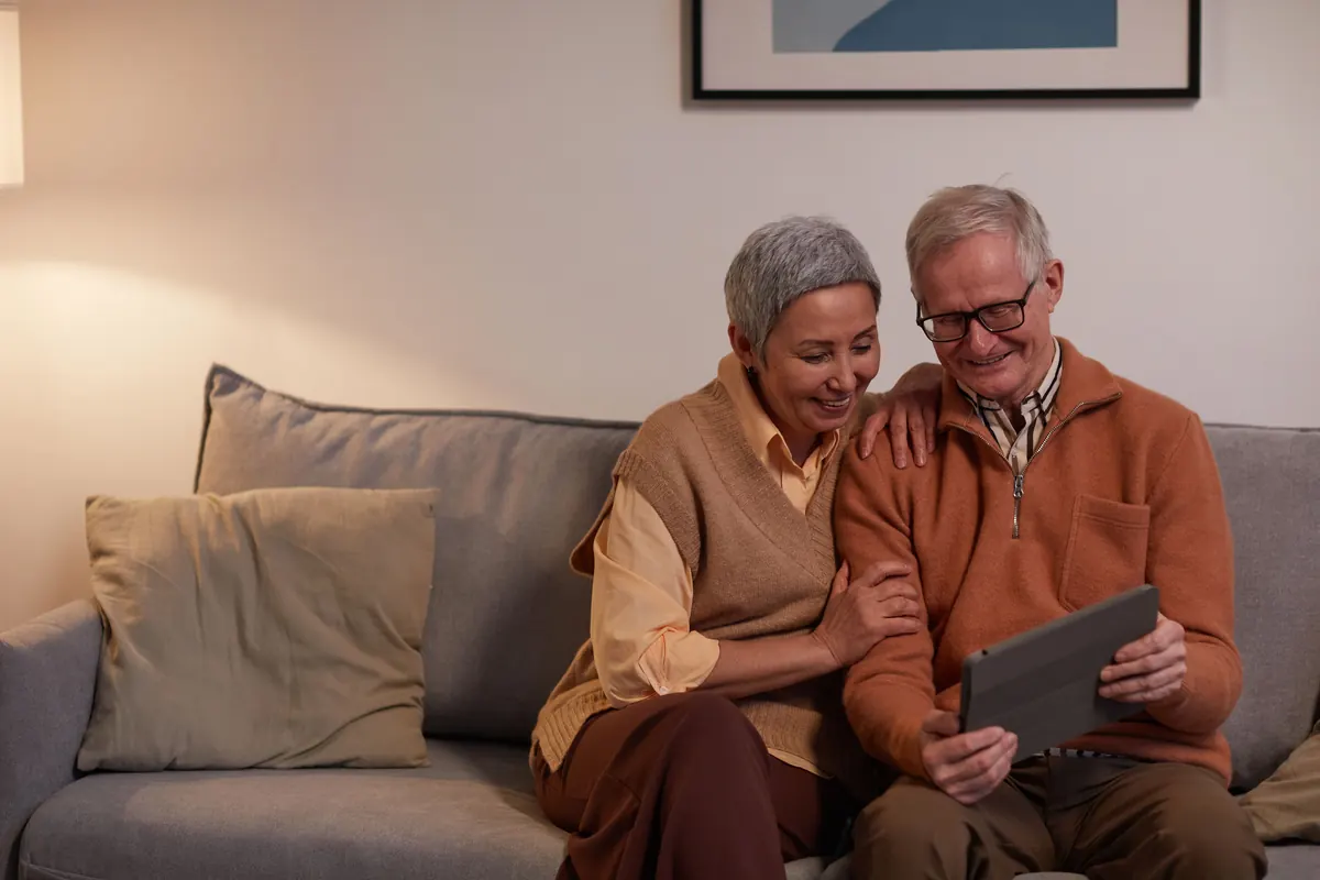 Zwei ältere Menschen betrachten gemeinsam ein Tablet auf dem Sofa. Stockfoto.